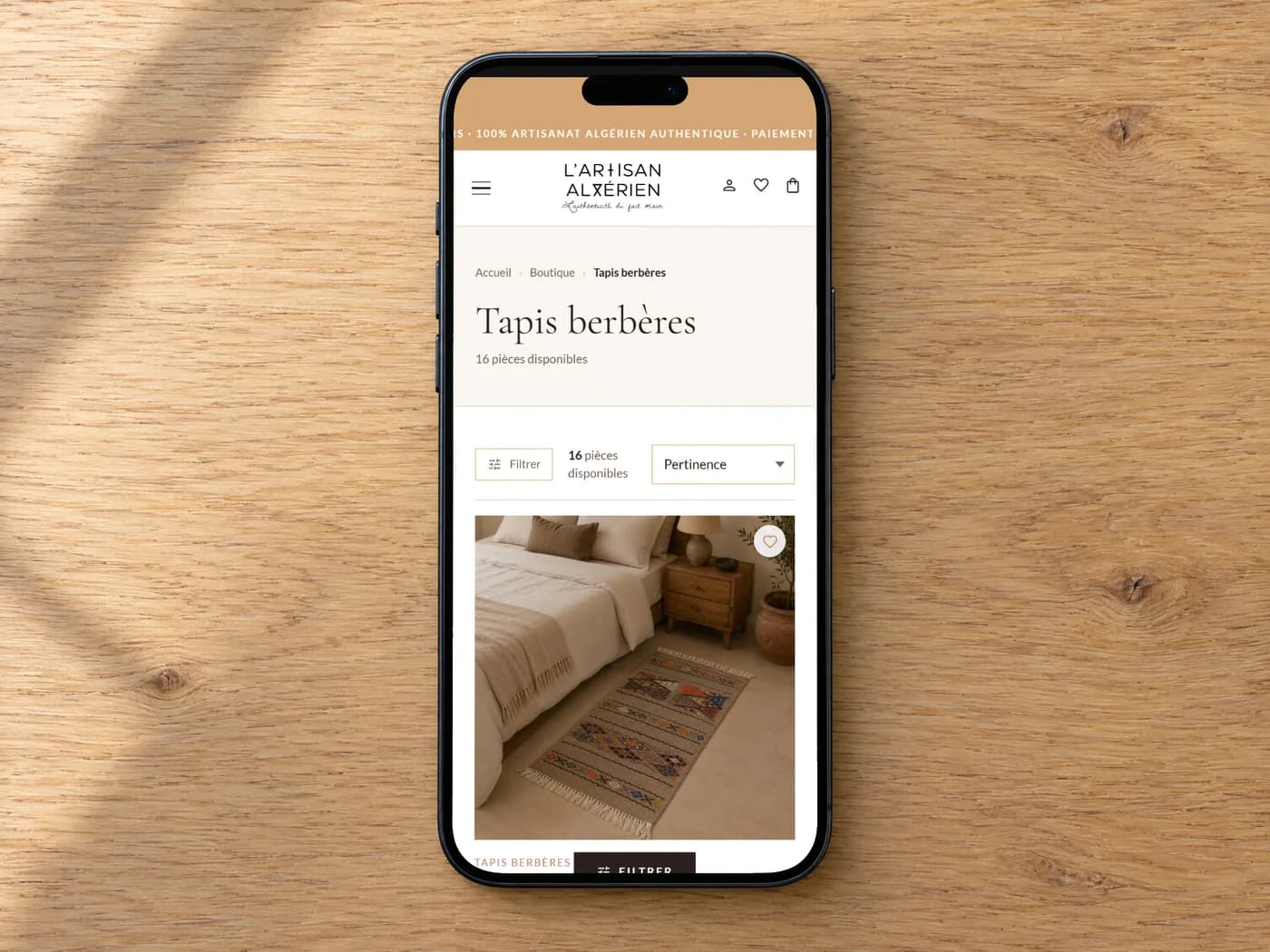 Un iPhone posé à plat sur une table en bois, affichant les tapis berbères de L'Artisan Algérien