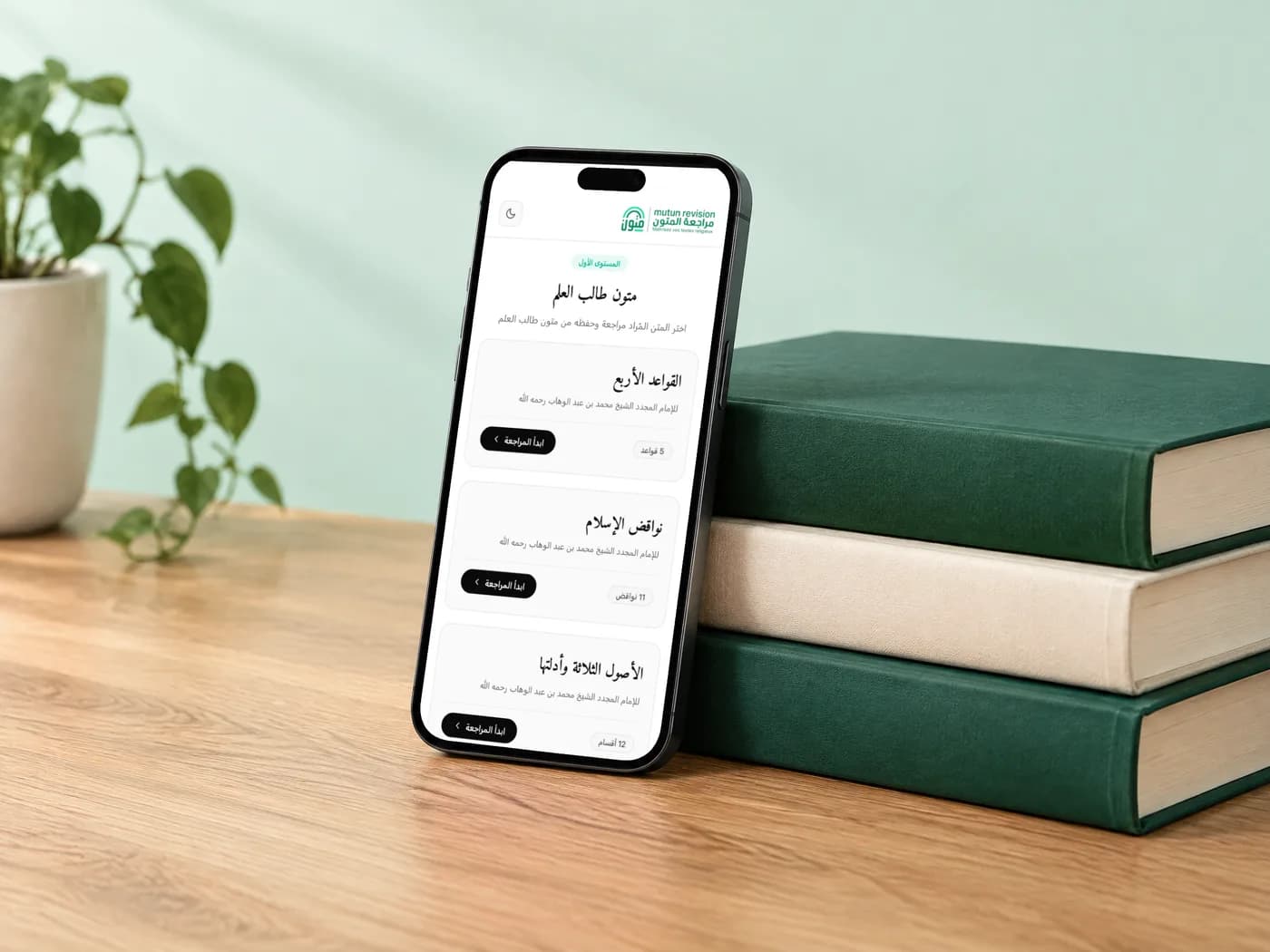 L'application Mutun Talib 3ilm sur un téléphone appuyé contre une pile de livres reliés verts